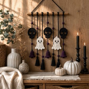 Peut inclure: Une décoration murale composée d'une tige en bois avec des cordons noirs suspendus. Les cordons portent trois crânes noirs au crochet, deux fantômes blancs au crochet, des perles violettes, des clochettes violettes et des pompons noirs.