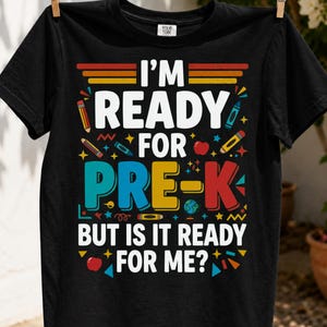 May include: A black short-sleeved t-shirt featuring the colorful text "I'M READY FOR PRE-K BUT IS IT READY FOR ME?" surrounded by graphic illustrations of pencils, crayons, a red apple, and a globe in shades of yellow, orange, red, and blue.
