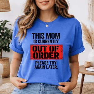 Pode incluir: Uma camiseta azul com o texto "THIS MOM IS CURRENTLY OUT OF ORDER PLEASE TRY AGAIN LATER" em preto e vermelho. A camiseta &eacute; de gola redonda.
