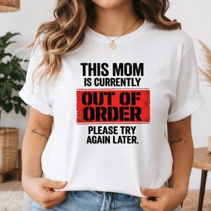 Pode incluir: T-shirt branco com o texto "THIS MOM IS CURRENTLY OUT OF ORDER PLEASE TRY AGAIN LATER" em preto e vermelho. A camisa tem mangas curtas e gola redonda.