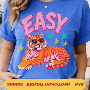 Puede incluir: Camiseta azul con la palabra "EASY" en rosa, encima de un tigre de dibujos animados con gafas de sol. El tigre es naranja y rosa con estrellas verdes y amarillas. La parte inferior de la camiseta tiene el texto "300DPI DIGITAL DOWNLOAD PNG".