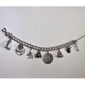 May include: A silver charm bracelet with various charms, including a high heel shoe, a rose, a butterfly, a cup, a round charm with text, a bell, a heart, and a key. The bracelet is on a white background.