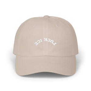May include: A beige baseball cap with the words "FUCK ICE" embroidered in white, arched across the front. The cap has a curved brim and a rounded crown. The hat is made of a soft material.