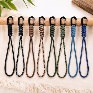 May include: Eight paracord lanyards with black carabiner clips, each featuring a different color or pattern including solid black, black with white flecks, solid brown, tan camouflage, solid olive green, green camouflage, light blue, and royal blue.