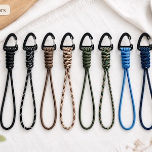 May include: Eight lanyards with black carabiner clips, each featuring a different cord style including solid black, black and white speckled, solid brown, tan camouflage, solid olive green, green camouflage, solid blue, and navy blue rope.
