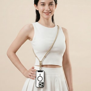 May include: A white smartphone case with a black circular MagSafe magnetic ring and a black camera module cutout. The case is attached to a long, thin, beige-colored cord strap that hangs diagonally across the torso, allowing the phone to be worn.