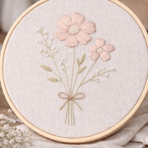 Peut inclure: Broderie florale sur cerceau, représentant un bouquet de fleurs roses avec des feuilles vertes et des accents blancs. La broderie est réalisée sur un tissu beige clair, encadrée par un cerceau en bois. Un projet artisanal délicat.