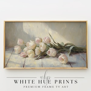 May include: A framed painting of a bouquet of white and pink tulips with green stems, lying on a light-colored wooden surface. The painting has a gold frame and the text "WHITE HUE PRINTS" and "PREMIUM FRAME TV ART" at the bottom.