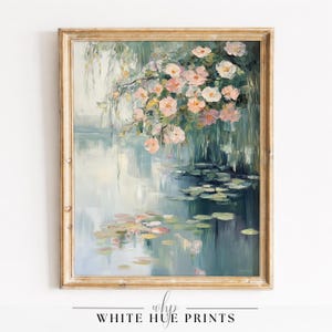 以下が含まれることがあります： 金色のフレームに入った絵画。このアートワークは、スイレン、柳、ピンクの花が描かれた穏やかな水辺の風景を描いています。「WHITE HUE PRINTS」の文字が下にあります。