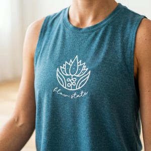 May include: Teal sleeveless tank top with a white floral design and the words "flow state" printed below. The tank top is made of a soft, textured fabric and has a round neckline.