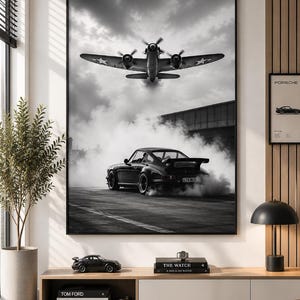 May include: A large black and white framed wall art print depicting a vintage airplane flying above a sports car drifting on a track, surrounded by thick smoke. The scene is captured in a high-contrast monochrome style, showcasing the vehicle's rear.