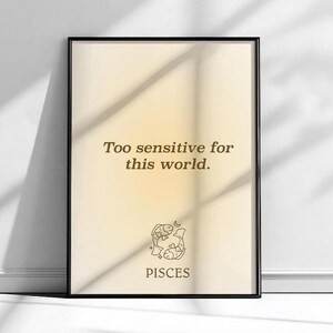 May include: Framed art print with a black border. The print features the text "Too sensitive for this world" in a brown serif font. Below the text is a line drawing of two fish and the word "PISCES". The background has a gradient of light yellow to white.