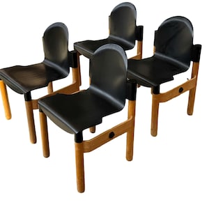 Puede incluir: Cuatro sillas negras con respaldos y asientos curvos. Las sillas tienen patas y marcos de madera de color claro, con detalles negros en las uniones. Las sillas están dispuestas en grupo, mostrando su diseño y estilo. Las sillas son adecuadas para un comedor o sala de estar.