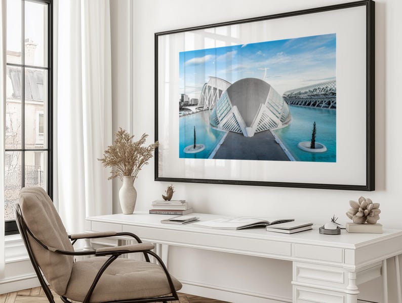 May include: A framed photograph of a modern architectural structure with a blue sky and water. The building has a unique, curved design with glass and white elements. The photograph is displayed on a white desk with a chair, vase, and other decorative items.