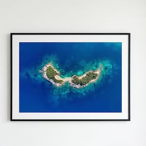 Pode incluir: Uma impressão emoldurada mostrando uma vista aérea de uma pequena ilha com vegetação verde exuberante, contra um fundo de oceano azul profundo. As bordas rochosas da ilha contrastam com as águas claras e turquesas. A impressão é emoldurada em preto.