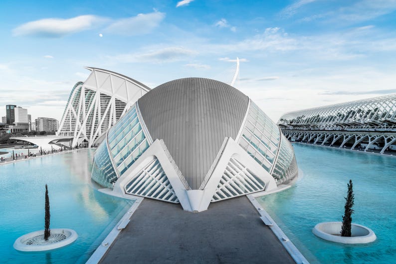 May include: Architectural photograph of the City of Arts and Sciences in Valencia, Spain. The image features modern, white, and gray structures with glass panels, set against a blue sky and water. The buildings have unique, curved designs.