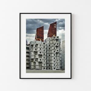 Può includere: Stampa architettonica con un edificio unico con unità impilate a forma di cubo e strutture del tetto color ruggine. L'edificio ha un design distintivo con finestre circolari e un cielo nuvoloso.