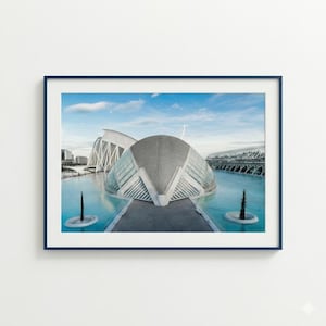May include: A framed print featuring a modern architectural complex with a distinctive, curved design. The buildings are set against a backdrop of a bright blue sky and water, creating a serene and contemporary aesthetic.