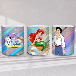 May include: Three white ceramic mugs featuring characters from Disney's "The Little Mermaid." One mug displays the movie title and characters, another features Ariel, and the third shows Prince Eric. Each mug has a colorful, iridescent background.
