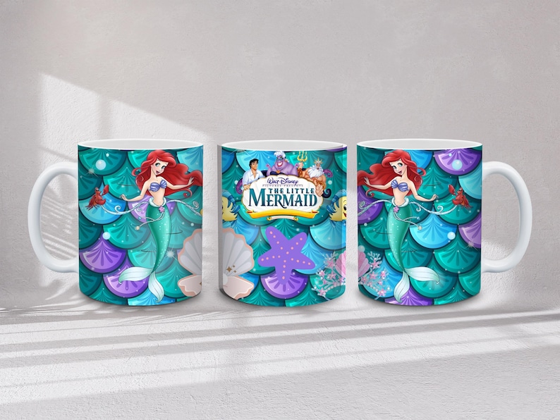 May include: White ceramic mug featuring Ariel from Disney's The Little Mermaid. The mug has a teal, purple, and blue scale pattern background. Ariel is depicted with red hair and a green tail. The mug has a white handle.