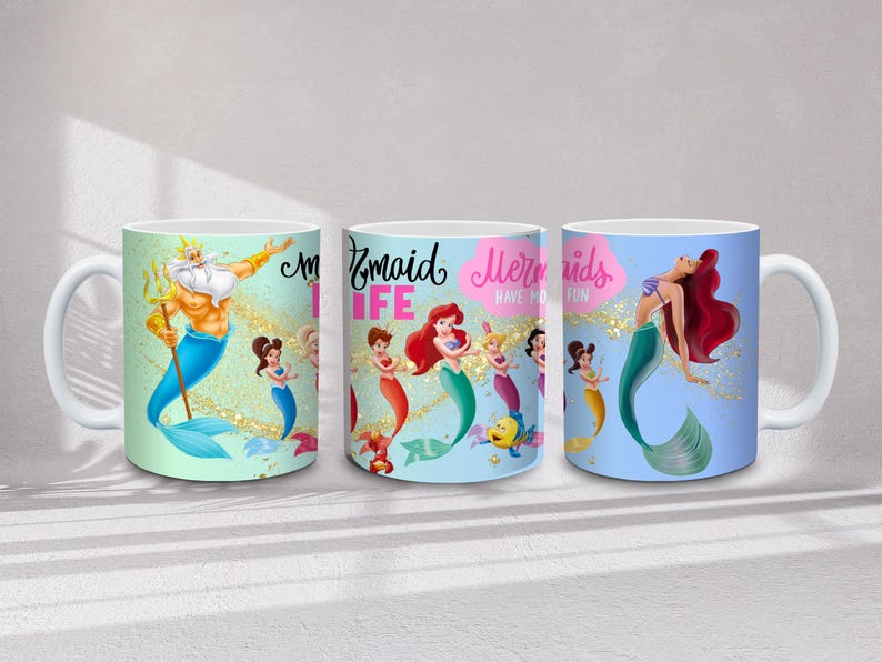May include: Three white ceramic mugs with mermaid-themed designs. One mug features King Triton, another displays mermaids with the text "Mermaid Life", and the third showcases a mermaid with red hair. Each mug has a white handle.