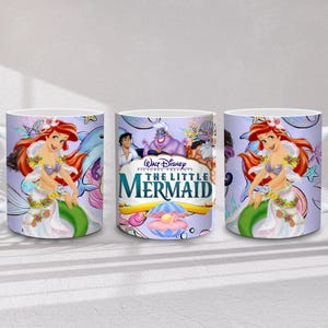 May include: White ceramic mug featuring Ariel from Disney's The Little Mermaid. The mug has a wraparound design with Ariel, a dolphin, and the movie's logo. The background is a light purple with stars and other sea creatures.