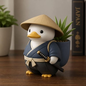 May include: A white duck figurine wearing a tan conical hat and a dark blue kimono with a beige sash. The duck carries a blue planter on its back containing a green succulent plant and holds a black and gold katana sword at its side.