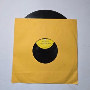 May include: A vintage vinyl record in a yellow paper sleeve. The record label is visible, featuring the text "Hank Williams" and "My Heart Would Know". The record is black, and the sleeve has a circular cutout.