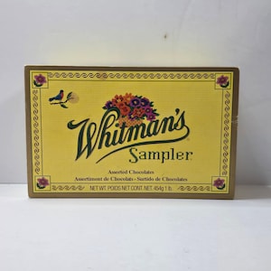 May include: A yellow box of Whitman's Sampler assorted chocolates. The box features a floral design and the brand name in a cursive font. The box contains 1 lb of chocolates, or 454g.