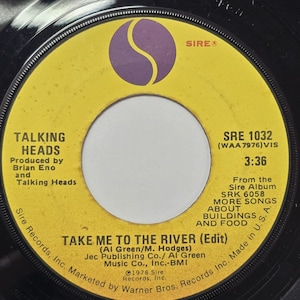 May include: A vintage vinyl record single by Talking Heads. The record label is yellow with black text, featuring the song title "Take Me to the River (Edit)". The Sire Records logo is visible, along with the album title "More Songs About Buildings and Food".