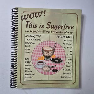 May include: A spiral-bound cookbook titled "Wow! This is Sugarfree." The cover features text and illustrations about sugar-free cooking, including a dessert in a glass, a cup of tea, and cookies. The book's design is vintage.