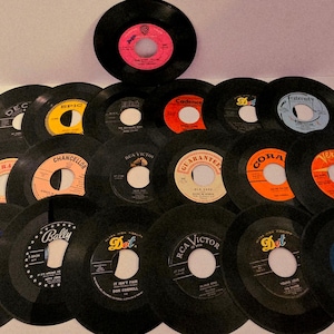 Könnte beinhalten: Eine Sammlung von Vintage-Vinyl-Schallplatten mit 45 U/min. Die schwarzen Schallplatten haben farbenfrohe Etiketten, darunter Orange, Gelb, Blau und Rot. Einige Etiketten zeigen Texte wie "Dot", "RCA Victor" und "Bally".