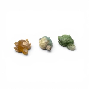 May include: Three carved stone turtle figurines in shades of amber, blue-green, and green. Each turtle has a detailed shell and head, with a smooth, polished finish. The figurines are displayed on a white background.