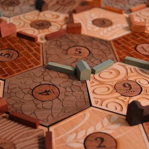 May include: Wooden board game with hexagonal tiles and wooden game pieces. The tiles are engraved with various patterns and numbers. The game pieces include small houses and roads in shades of brown, red, and green.