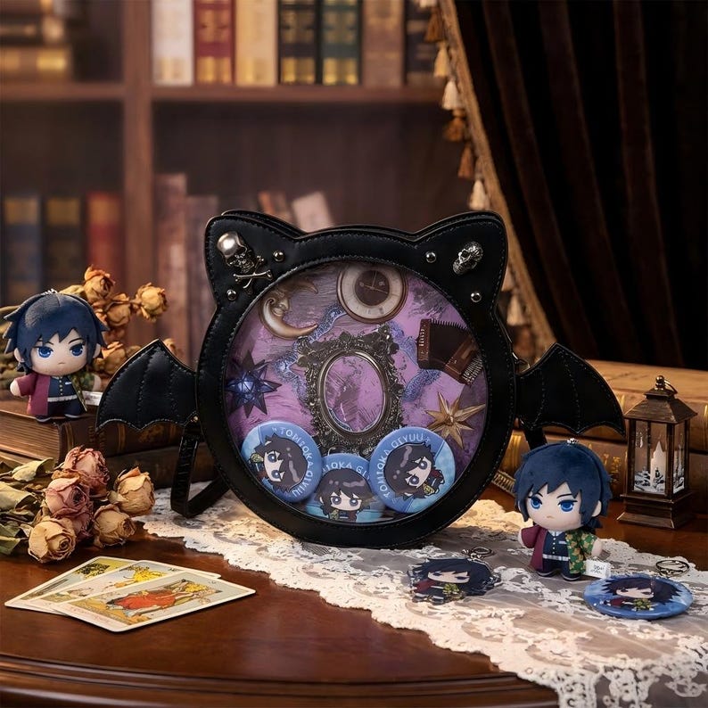 K&ouml;nnte beinhalten: Eine schwarze fledermausf&ouml;rmige Handtasche mit einem transparenten Sichtfenster, verziert mit Totenkopf-Akzenten. Im Inneren eine dekorative Anordnung von himmlischen und antiken Elementen. Enth&auml;lt Charakter-Pl&uuml;schtiere, Kn&ouml;pfe und Schl&uuml;sselanh&auml;nger, alles auf einem Holztisch.