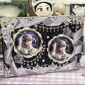 May include: A decorative black frame with two circular portraits featuring a man with gray hair. The frame is adorned with silver lace, ribbons, and faux roses. The portraits have the text "HAPPY BIRTHDAY".