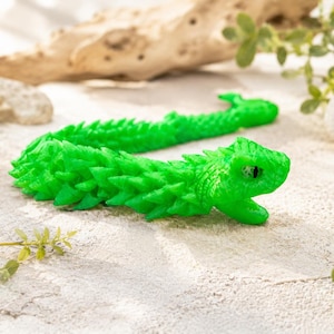 Könnte beinhalten: Zwei hellgrüne, bewegliche Drachenspielzeuge liegen auf einer strukturierten Oberfläche, mit einem natürlichen Hintergrund im Freien. Die Drachen haben detaillierte Schuppen und offene Münder. Die Spielzeuge sind leuchtend grün.