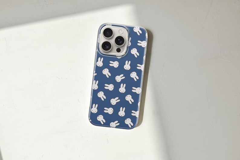 Puede incluir: Funda transparente para tel&eacute;fono con fondo azul y un patr&oacute;n de caras de conejos blancos. La funda tiene un borde transparente y cubre la parte trasera y los laterales del tel&eacute;fono, con recortes para la c&aacute;mara y los botones.