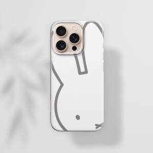 Puede incluir: Funda de tel&eacute;fono blanca con un contorno gris de un conejo. El dise&ntilde;o minimalista destaca la silueta y los rasgos faciales del conejo. La funda tiene un borde transparente y un m&oacute;dulo de c&aacute;mara.