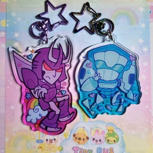 May include: Two keyrings with cartoon character designs. One keyring features a purple character with a rainbow and hearts, the other a blue character. Two star-shaped keyrings are also visible.