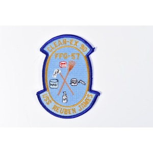 May include: A blue and gold embroidered patch with the text "CLEAN-EX 90" and "USS REUBEN JAMES". The patch features a light blue center with various illustrations, including a paint can, a brush, and the text "WAX".