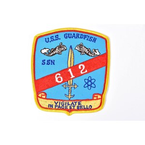 May include: Embroidered patch with a blue background featuring the text "U.S.S. GUARDFISH" and "SSN 612". The patch includes a red stripe, a sword, and two fish-like creatures. The bottom has the text "VIGILATE IN PACE ET BELLO".