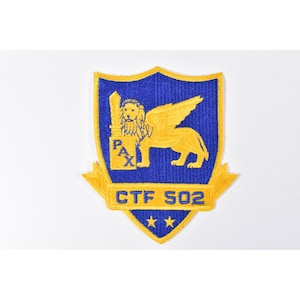 May include: Embroidered patch with a blue shield shape and a gold winged lion design. The patch features the text "PAX" and "CTF 502" in gold, along with two gold stars at the bottom. The patch is on a white background.