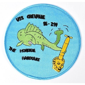 May include: Embroidered patch with a light blue background featuring a green cartoon fish, a yellow torpedo, and the text "USS GREVALLE SS-291" and "THE HORRIBLE HARDTAKS" in black.
