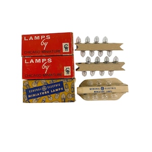 May include: Vintage miniature lamps in original packaging. Two red boxes read "LAMPS by CHICAGO MINIATURE." A blue and yellow box reads "GENERAL ELECTRIC MINIATURE LAMPS." Several clear light bulbs are visible.