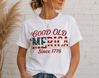 May include: White t-shirt with the text "GOOD OLD 'MERICA Since 1776" in red, white, and blue. The shirt features a classic crew neck and short sleeves. The design incorporates the American flag colors and patriotic theme.