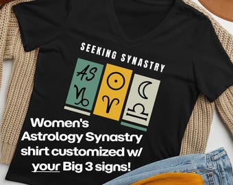 May include: A black V-neck t-shirt featuring the text SEEKING SYNASTRY above three rectangular panels in muted green, yellow, and light green. The panels display astrological symbols for the sun, moon, and rising signs in black ink.