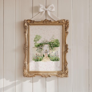 May include: A framed watercolor print of a garden scene, featuring a path leading to an archway covered in flowers. The ornate gold frame is suspended by a white ribbon tied in a bow. The background is a white wall.