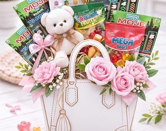 May include: A white purse-shaped gift basket filled with lottery tickets, a teddy bear, candy, and pink flowers. The basket has a gold tassel and handle details. Gummy candies and flower petals are scattered around the base.