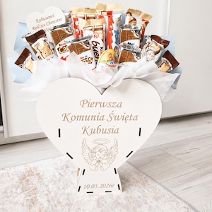Könnte beinhalten: Ein Geschenkarrangement mit verschiedenen Schokoriegeln und Süßigkeiten, präsentiert in einem herzförmigen Holzhalter. Der Halter hat Text und eine Engel-Illustration. Das Arrangement befindet sich auf einer hellen Oberfläche.